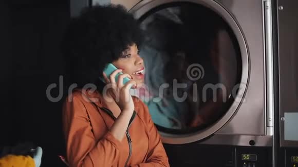 微笑的年轻女子在洗衣店用手机交谈视频的预览图