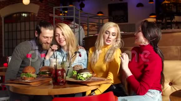 漂亮的女孩和开朗的男孩坐在一起吃汉堡视频的预览图