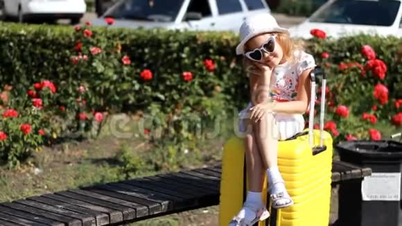小女孩游客坐在一个大黄色的手提箱上等待旅行的儿童视频的预览图