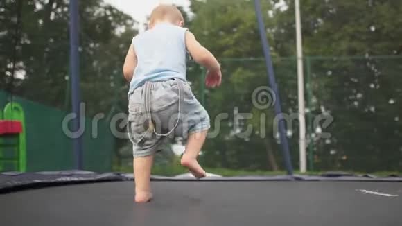 一个金发小男孩在公园的蹦床上慢动作跳着视频的预览图