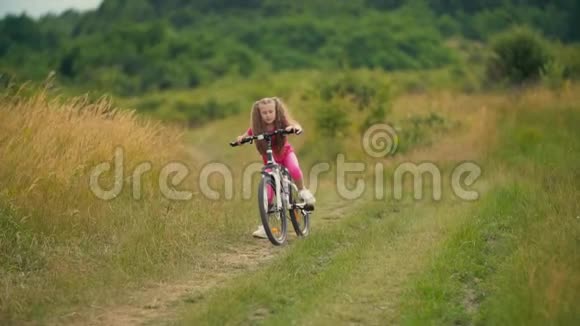 女孩骑自行车在长满青草的马路上视频的预览图