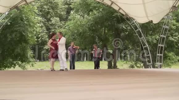 手风琴和小提琴在公园里演奏一个穿红色衣服的女人和一个穿白色西装的男人正在跳探戈老年人视频的预览图