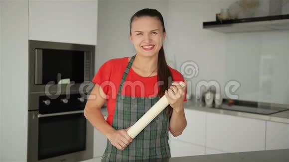 厨房背景上年轻微笑女孩的肖像她拿着擀面杖看起来真高兴视频的预览图