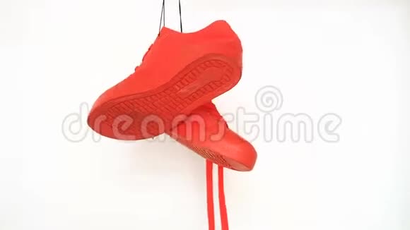 白色背景上挂着一双红色运动鞋橙色的靴子在绳子上旋转视频的预览图