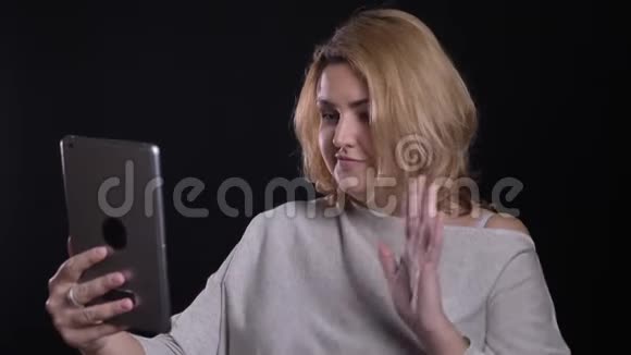 可爱的金发短发超重的女商人在黑色背景的平板电脑上愉快地在视频聊天视频的预览图