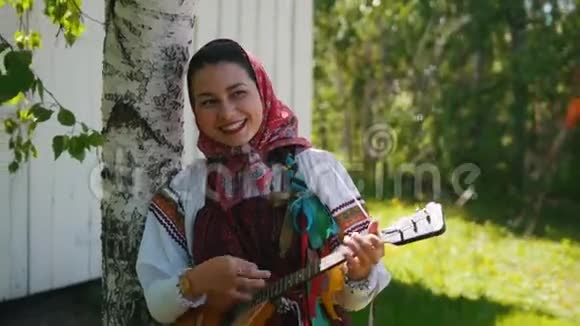 穿着俄罗斯传统服装的年轻女性站在森林里玩巴拉莱卡视频的预览图