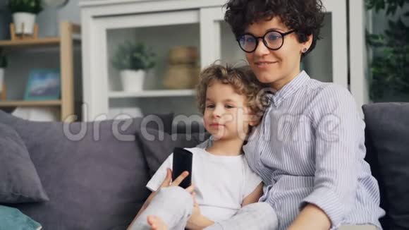 可爱的男孩和母亲年轻的女人在沙发上看电视和在家聊天视频的预览图