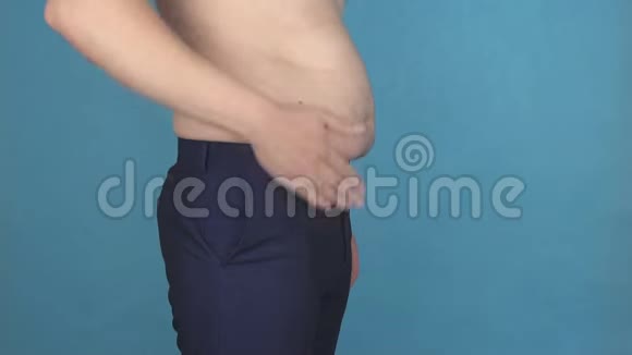 一个年轻人在蓝色背景下拍着肥胖的胖肚子肥胖和肥胖问题的概念视频的预览图
