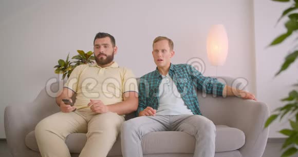 两名在电视上观看足球比赛的白种人的特写照片他们因坐在沙发上而沮丧视频的预览图