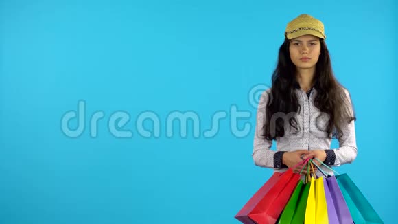 手里拿着袋子的购物狂女孩站着开始微笑蓝色背景视频的预览图