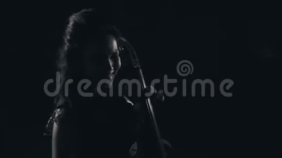 一个情绪化的女孩在黑暗的房间里玩大提琴很美的光大提琴手的特写视频的预览图