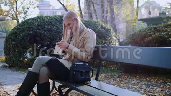 女孩用智能手机在城市公园的长凳上交流视频的预览图