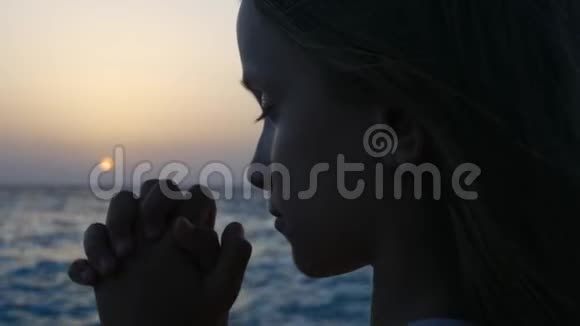 日落时在海滩上祈祷的孩子体贴的祈祷孩子海边的沉思女孩视频的预览图