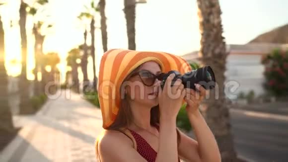 摄影女游客戴着一顶黄色的大帽子在夕阳下美丽的热带风景中用相机拍照视频的预览图