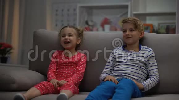 快乐的孩子们坐在沙发上看喜剧片玩得开心一起笑视频的预览图