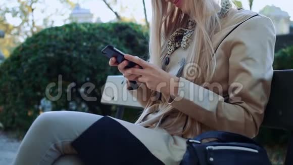 有智能手机的女人在秋天的公园枫树上放松坐在长凳上的女孩视频的预览图