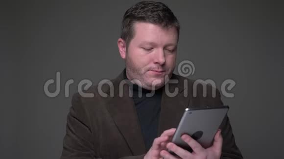 布鲁内特中年商人穿着西装在平板电脑上冲浪对灰色背景有情感反应视频的预览图