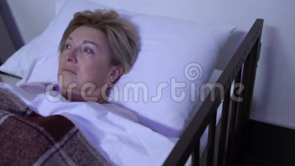 沮丧的老年妇女躺在电视机前病床上想着疾病视频的预览图