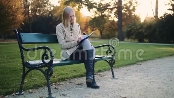 美丽的年轻女子正在公园的户外写日记视频的预览图