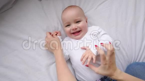 穿着白色t恤的宝宝躺在一张白色的床上笑着看着镜头前的慢镜头视频的预览图