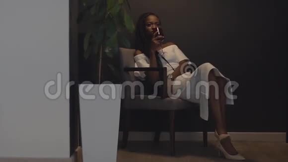 年轻美丽的非洲裔美国女性时尚模特坐在舒适的椅子上喝着红酒杯视频的预览图