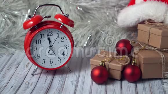 红色老式闹钟和木制桌子上的三个礼品盒上面装饰着花环和红色圣诞球视频的预览图