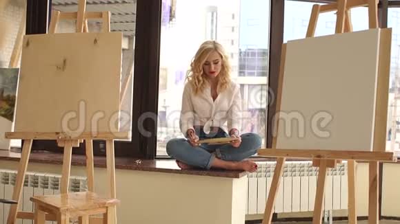 性感的艺术家坐在窗台上手里拿着画笔和调色板视频的预览图