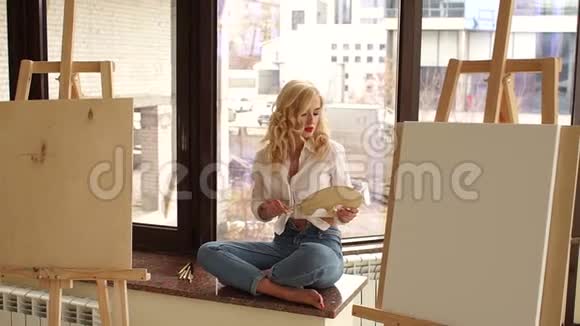 性感的艺术家坐在窗台上手里拿着画笔和调色板视频的预览图