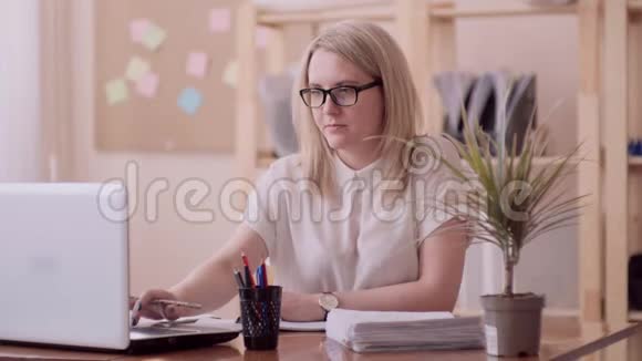 白种人的金发女孩戴着眼镜右手在办公室里在花的右边坐着视频的预览图