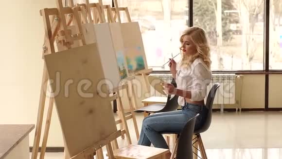 一个穿着白色衬衫的年轻性感女孩在画室的画布上画画视频的预览图
