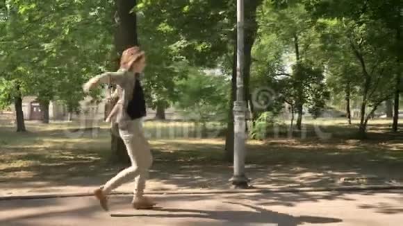年轻漂亮的女孩白天在公园的小路上跳舞夏天在公园里跳舞动作概念侧视娃娃镜头视频的预览图