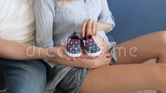 爸爸在怀孕妻子的肚子旁边抱着婴儿的鞋子可爱的框架与幼儿鞋视频的预览图