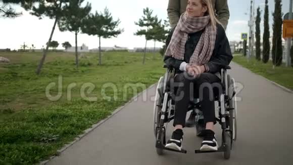 年轻的生病的女人坐在轮椅上男人在帮助她翻滚视频的预览图
