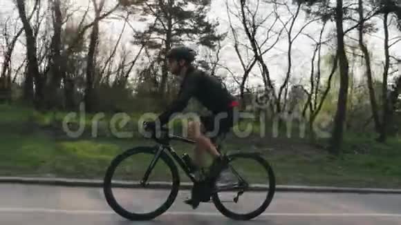 骑自行车的人穿着黑色运动衫穿着短裤在公园里骑着一辆黑色职业道路自行车侧跟射击自行车的概念慢慢视频的预览图