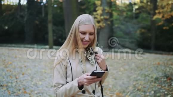 年轻的金发女孩走在秋天的公园里把金色的叶子扔到空中慢动作视频的预览图
