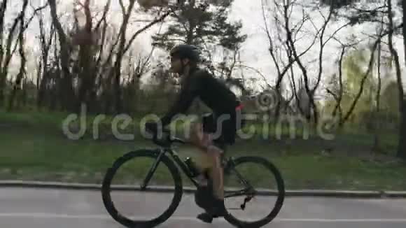 骑自行车的人穿着黑色运动衫穿着短裤在公园里骑着一辆黑色职业道路自行车侧跟射击自行车的概念视频的预览图