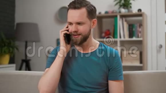 一个英俊的男人正在打电话在家笑着快乐留胡子的男人穿着休闲的室内肖像盖盖视频的预览图