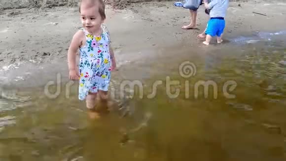 一个小女孩穿着花裙子站在岸边的水中很高兴视频的预览图