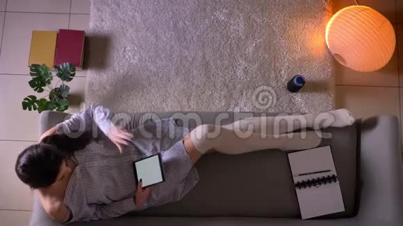 在平板电脑上穿着可爱的袜子坐在沙发上看电子书的年轻迷人的女青少年特写镜头视频的预览图