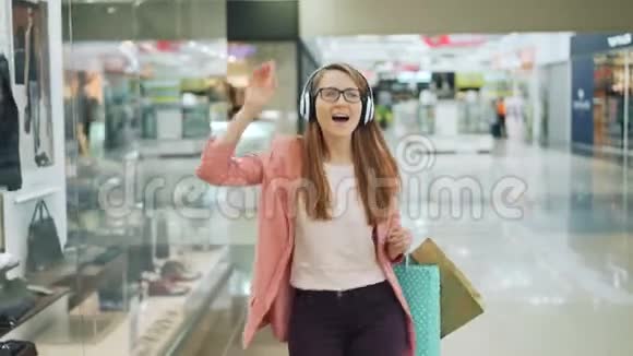 免费的年轻女学生正在购物中心听音乐戴着耳机跳舞唱歌享受着快乐视频的预览图