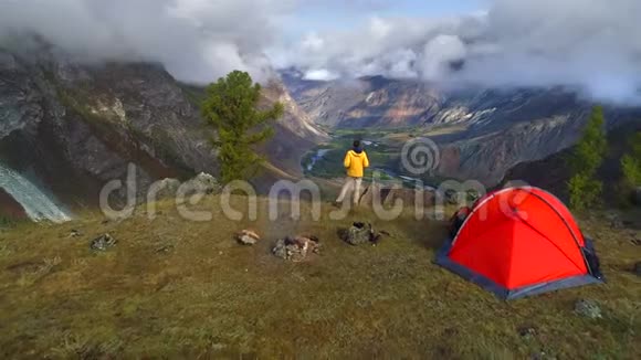 一名男子站在山谷前的帐篷附近的空中镜头视频的预览图