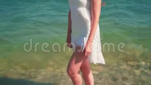 一个穿着白色海滩礼服的女孩沿着海滨散步一个光着脚的漂亮女孩沿着海滨散步视频的预览图