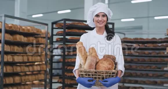 面包师夫人带着美丽的微笑手里拿着一个篮子里面有新鲜的烘焙面包直视着面包店里的摄像机视频的预览图