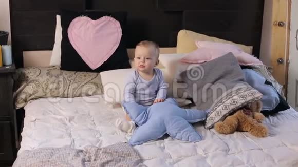 小可爱的一岁男孩坐在床上铺着一条蓬松的毯子视频的预览图