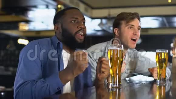 两个年轻人在酒吧里看体育比赛碰杯啤酒爱好视频的预览图