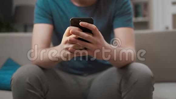 高加索人使用现代移动智能手机坐在家里的沙发上双手拿着手机视频的预览图