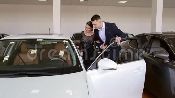 年轻夫妇在经销商的展厅里看一辆新的白色汽车视频的预览图