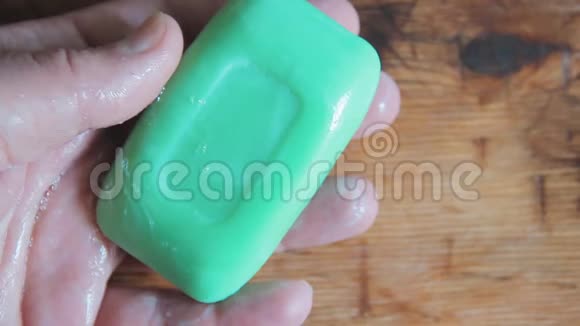 一个男人把一块绿肥皂放在湿手掌里拉手浴室准备清洗背景木材纹理视频的预览图