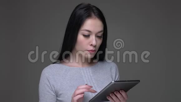在平板电脑上拍摄白种人白种人年轻漂亮的女性短信特写镜头背景是灰色的视频的预览图