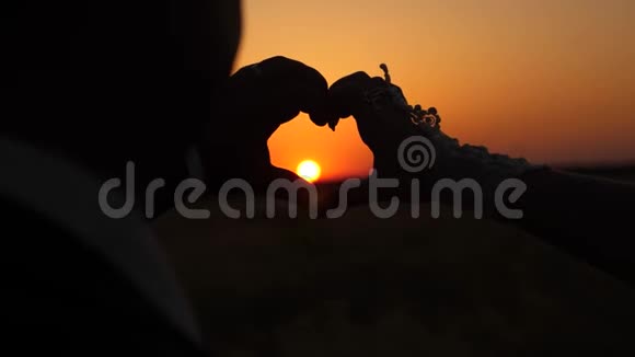 女人和男人用手在地平线上美丽的日落前做心脏标志太阳在手里团队合作视频的预览图
